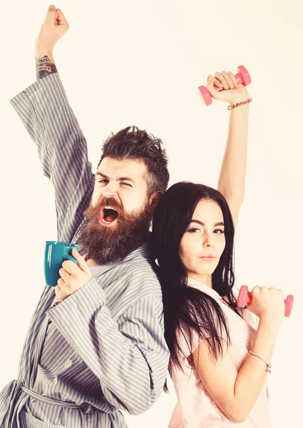 Couple amoureux en pyjama, peignoir dos à dos. Concept d'énergie matinale. Fille avec haltère, homme avec tasse de café, isolé sur fond blanc. Couple, en famille sur des visages endormis, s'étirer — Photo