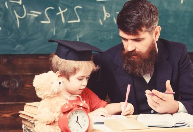 İlk öğretim. Öğretmen formal giyim ve öğrenci sınıfta kolej, kara tahta arka plan. Öğretmen ile eğitim evlat. Baba oğul, öğretir tartışmak, açıklamak. Eğitim kavramı