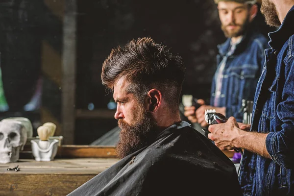 Barbiere con acconciatura a clipper di brutale cliente barbuto. Concetto di stile di vita hipster. Il barbiere con tagliacapelli lavora sull'acconciatura per lo sfondo del barbiere. cliente hipster ottenere taglio di capelli — Foto Stock