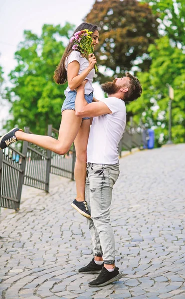 Typ, der Freundin aufzieht. romantischer Date-Spaziergang. glücklich, sie zu sehen. Mann trägt Freundin in Händen, während sie Blumenstrauß auf l romantisches Date hält. Verliebtes Paar trifft sich zum Date im Park — Stockfoto