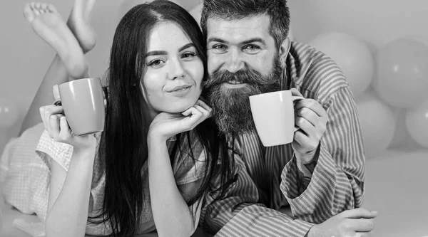Homme et femme sur des visages souriants gisaient, fond rose. Couple se détendre le matin avec du café. Couple amoureux boire du café au lit. Concept de tradition familiale. Homme et femme en vêtements domestiques, pyjama — Photo