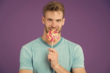 Ölmek hakkında kimin umurunda. Adam büyük tatlı lolipop ısırır. Adam kıl ile tatlılar seviyor. Şımarık diyet. Sporcu yüz gülümseyen üzerinde renkli lolipop, menekşe arka plan yiyor. Yemek kavram hile