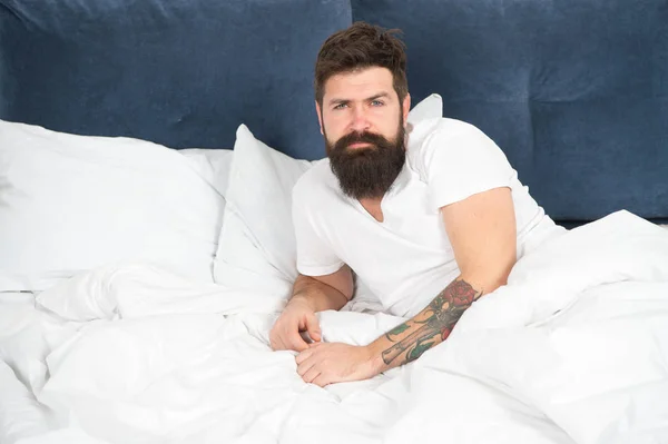 Lo primero que haces después de despertar. Hombre barbudo hipster somnoliento cara relajarse en la cama. Por la mañana temprano. Relájate y duerme. El hombre barbudo duerme en sábanas blancas. Sueño saludable y bienestar —  Fotos de Stock