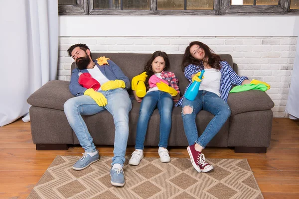 Finish cleaning. Cleaning all day exhausting occupation. Tired parents and kid. Exhausting cleaning day. Family mom dad and daughter with cleaning supplies sit on couch. Family care about cleanliness