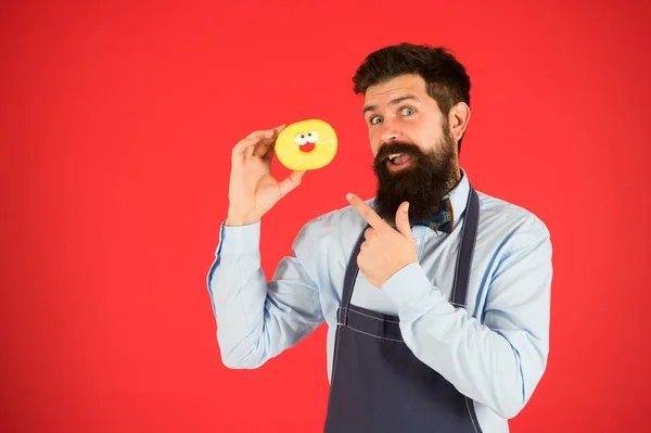 Comida de batota. Hipster padeiro barbudo segurar donut vitrificado no fundo vermelho. Conceito de café e padaria. Doce donut do padeiro. Homem padeiro barbudo no avental de cozinha segurar sobremesa bonito. Esqueça a dieta — Fotografia de Stock