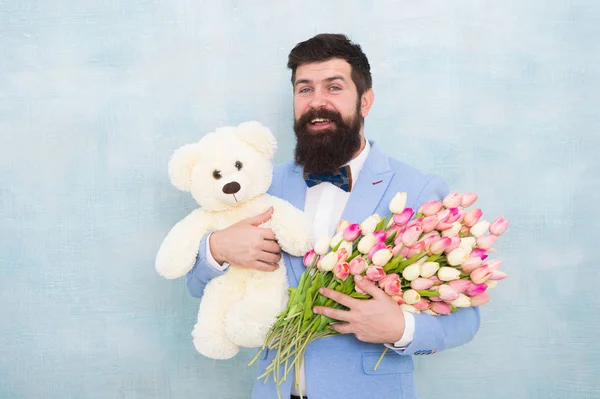 Feliz y enamorada. Hombre barbudo caballero traje pajarita agarre osito de peluche y ramo. Caballero haciendo una sorpresa romántica para ella. Un regalo romántico para caballeros. Saludos de cumpleaños. Feliz cumpleaños mi amor —  Fotos de Stock