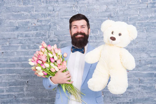 Macho getting ready romantic date. Man wear blue tuxedo bow tie hold flowers bouquet. International womens day. Surprise will melt her heart. Romantic man with flowers and teddy bear. Romantic gift