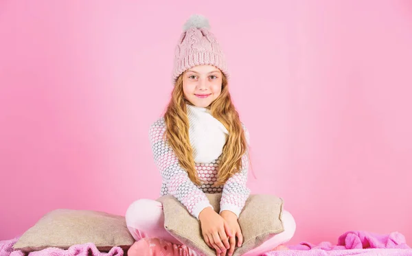 Χειμερινή μόδα έννοια. Μακριά μαλλιά κορίτσι χαλάρωση ροζ φόντο. Χειμερινή μόδα για τα παιδιά. Μοντέλο μόδας χαμογελαστό παιδί. Παιδί κορίτσι φορούν χαριτωμένο πλεκτό καπέλο μοντέρνα και άνετα ζεστά ρούχα — Φωτογραφία Αρχείου