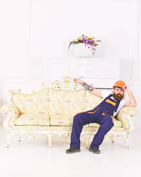 Bearded worker sitting on antique sofa isolated on white background. Tired mover enjoying small break from work