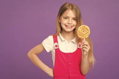 Sopa ya da lolipop büyük şeker kız. Tatlı çocukluk kavramı. Uzun saçlı çocuk tatlılar sever ve davranır. Yüz gülümseyerek kıza dev renkli lolipop el, menekşe arka planda tutar.