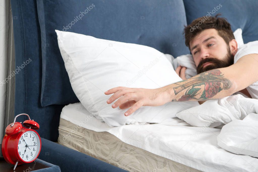 Tips for waking up early. Man bearded hipster sleepy face bed with alarm clock. Turn off that ringing. What terrible noise. Problem early morning awakening. Get up with alarm clock. Overslept again