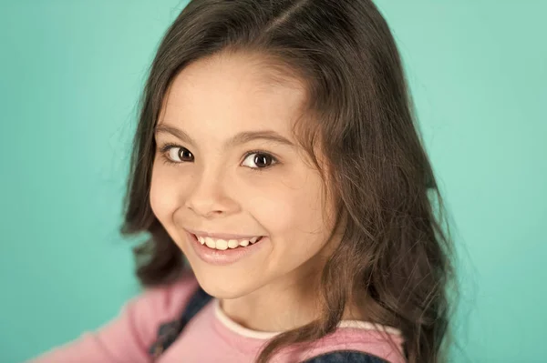 Ragazza felice con lunghi capelli castani sani su sfondo blu. Bambino con un sorriso sul viso adorabile. Salone di bellezza. Cura della pelle. La bellezza è potere, il sorriso è la sua spada — Foto Stock