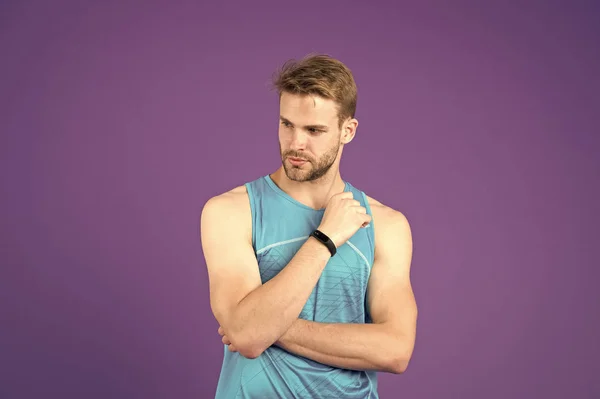 Deportista con peinado de moda y barba. Chico sexy haciendo ejercicio en el gimnasio, concepto de salud y fitness. Atleta en chaleco azul aislado sobre fondo púrpura. Hombre con dispositivo electrónico para entrenar en su muñeca —  Fotos de Stock