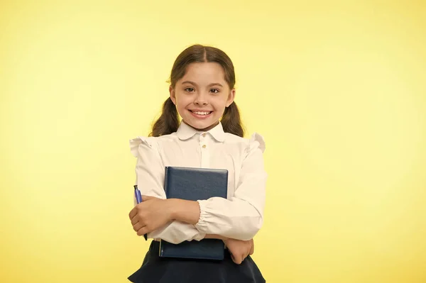 Készen állok az iskolára. Gyerekiskolai egyenruha, okos gyerek, kész a házi feladat. Lány aranyos boldog arc sárga háttér. Gyermek lány iskolai egyenruha tartja könyv és toll. Vissza az iskolába — Stock Fotó
