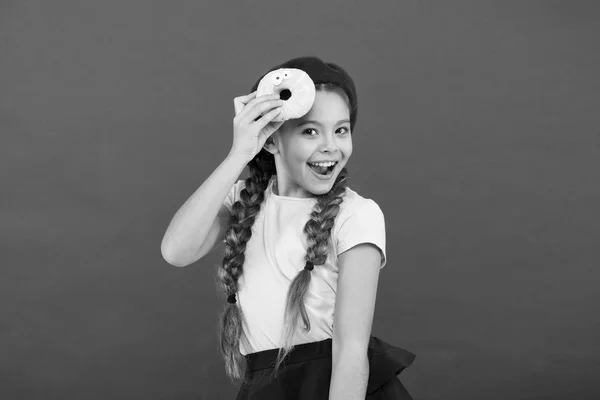 Impossible to resist fresh made donut. Girl hold glazed cute donut in hand red background. Kid playful girl ready to eat donut. Sweets shop and bakery concept. Kids huge fans of baked donuts — Stock Photo, Image