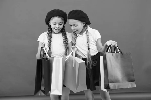 Shopaholic koncepcja. Oznaki, że jesteś uzależniony od zakupów. Ładny uczennice dzieci trzymać kilka toreb z zakupami. Dzieci uczniowie zadowolony przez zakupy czerwonym tle. Obsesję na punkcie zakupów i odzież centrów handlowych — Zdjęcie stockowe