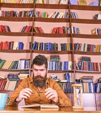 Adam meşgul yüz kitap okumak, kitap rafı arka plan üzerinde. Eğitim ve bilim kavramı. Bilim adamı, gözlük ve kum saati ile masada oturur. Öğretmen ya da sakal Kitaplığı'nda eğitim ile öğrenci