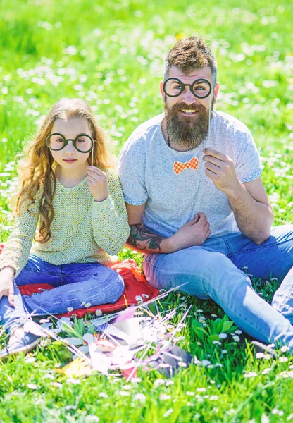 O pai e a filha sentam-se na relva no campo, fundo verde. Criança e pai posando com óculos atributos de cabine de fotos no prado. Família passar o lazer ao ar livre. Conceito inteligente e inteligente — Fotografia de Stock