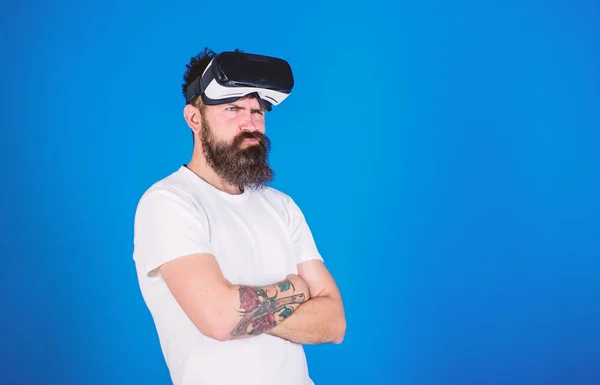 Man with long beard wearing VR headset over blue background. Bearded hipster with distrustful look ready to try new experience. Brutal macho with stylish beard skeptical about digital technologies