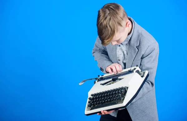 Yazarak makinasıyla. Küçük çocuk üzerinde eski daktilo typewriting. Vintage daktilo ile akıllı okul çocuğu. Daktilo ile sevimli çocuk. Küçük çocuk holding retro daktiloda mavi arka plan, kopya alanı — Stok fotoğraf