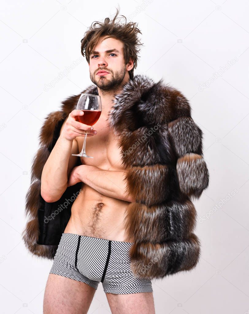 Rich athlete enjoy his life. Sexy sleepy rich macho tousled hair drink wine isolated on white. Fashion and pathos. Richness and luxury concept. Guy attractive rich posing fur coat on naked body