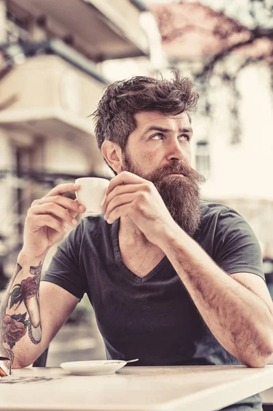 Koffiepauze concept. Bebaarde man houdt espresso kop, drinkt koffie op het terras. Man met lange baard ziet er dromerige. Man met baard en snor op kalm of dromerige gezicht, stedelijke achtergrond, intreepupil — Stockfoto