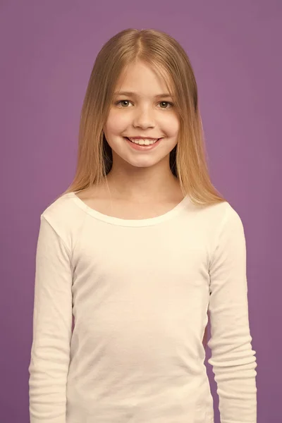 女孩在微笑的面孔与长的头发穿白色衬衣, 紫罗兰色背景。长头发的小女孩看起来很可爱。发型和头发护理的概念。女孩喜欢看起来可爱, 时髦和时尚 — 图库照片