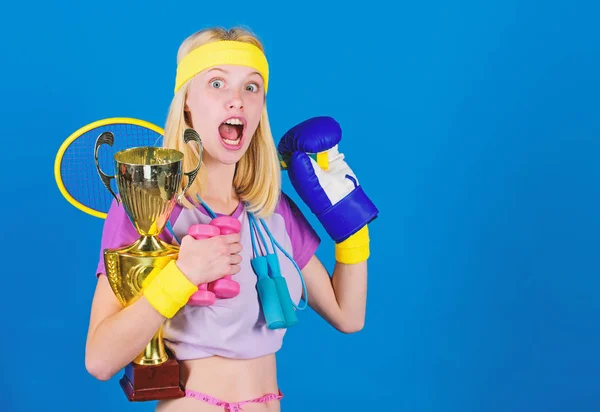 Desporto para todos os dias. Variedade de lojas de desporto. Menina bem sucedida mulher moderna segurar cálice de ouro do campeão do esporte e equipamento de fundo azul. Como encontrar tempo para tudo. Loja de equipamentos desportivos — Fotografia de Stock