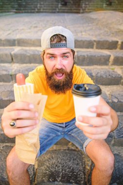 Fast food öğle yemeği ortak fikir için. Hipster sosisli sandviç içki kağıt bardak tadını çıkarın. Beslenme sorunları sokak gıda ile ilgili. Sakallı adam hızlı öğle yemeği merdiven arka plan tadını çıkarın. Hipster yemek sıcak köpek kahve