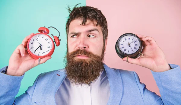 Mannen skäggig hipster håll två olika klockor. Guy orakad förbryllad ansikte har problem med att ändra tiden. Föränderliga tidszoner påverka hälsa. Tidszon. Gör ändra klockan bråka med din hälsa — Stockfoto