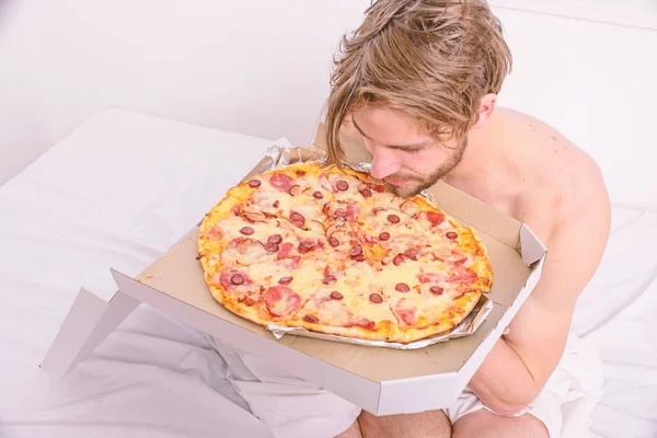 Pria suka pizza untuk sarapan. Sarjana nutrisi. Pria berjenggot tampan makan makanan murahan untuk sarapan di tempat tidur. Pria memegang kotak pizza duduk di tempat tidur di kamar tidur atau kamar hotel. Layanan pengiriman makanan — Stok Foto