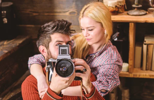 Hipster holding vintage camera while girlfriend hugs him. Vintage photographer concept. Couple in love spend romantic evening in warm atmosphere. Couple hugs in wooden vintage interior