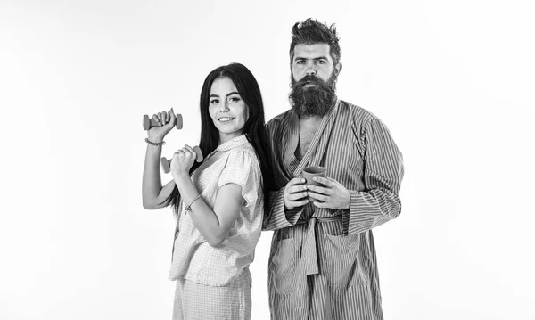 Couple amoureux en pyjama, peignoir isolé sur fond blanc. Couple, famille au visage endormi, pleine d'énergie. Fille avec haltère, homme avec tasse de café. Concept de routine matinale — Photo