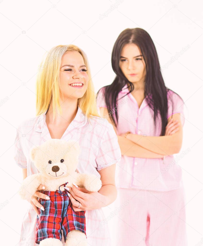 Girls in pink pajamas, isolated white background. Jealousy and envy concept. Sisters in pajamas looks unfriendly, jealous. Lady jealous to sister with plush toy bear, defocused