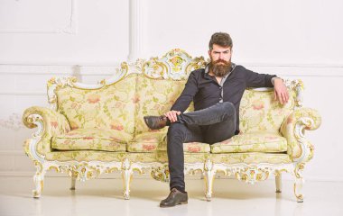 Hipster sıkı yüzünde yalnız oturuyor. Zengin ve yalnız kavramı. Lüks daire sahibi beyaz duvar arka koltukta oturur. Sakallı ve bıyıklı lüks oturma odasında boş zaman harcıyor