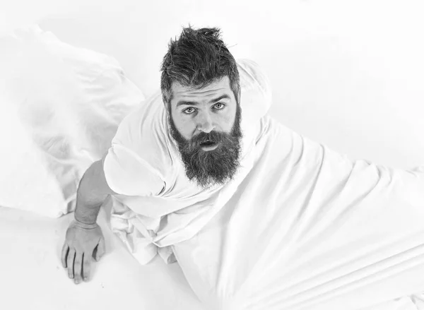 Man with sleepy face sit in bed, white sheets