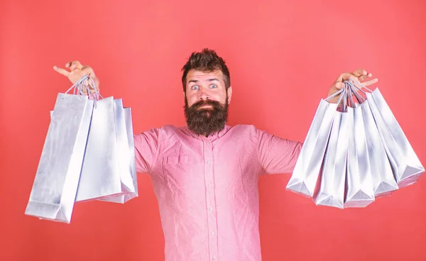 Szakállas férfi döbbenve a mennyiségű dolgot vásárolt eladó, vásárlás koncepció. Csípő a meglepett arcát és hosszú szakálla rózsaszín inget visel. Szakállas ember tartja ezüst papír táskák, divatos Store — Stock Fotó