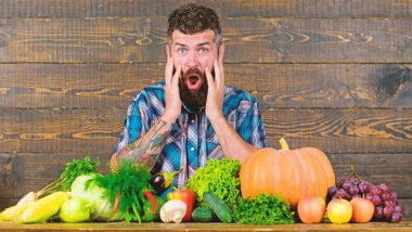 Çiftçi masada homegrown bitkileri ile. Sebze organik hasat. Çiftçi parlak sebze yüzünden şok. Tarım ve kavram hasat. Hasat ahşap arka plan bakmak sakallı adam