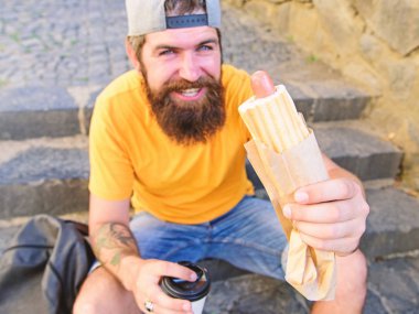 Hipster merdivenlerde açık havada sit süre sosisli sandviç ye. Senin yemek kavramı tadını çıkarın. Sakallı adam hipster sokak gıda kentsel arka plan tadını çıkarın. Kent gıda kültür kavramı. Lezzetli sosisli sandviç sosis roasty topuz