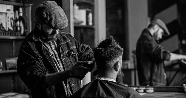 Réflexion du coiffeur avec tondeuse coupe les cheveux du client. Un client hippie qui se fait couper les cheveux. Concept de mode de vie hippie. Barbier avec tondeuse à cheveux travaille sur la coupe de cheveux du gars barbu, fond de salon de coiffure — Photo