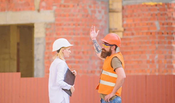 Woman engineer and bearded brutal builder discuss construction progress. Construction project management. Building industrial project. Discuss progress project. Construction industry concept