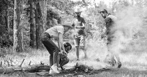 Company friends or family making bonfire in forest nature background. Friends working as team to keep bonfire. Company camping forest prepare bonfire for picnic. Add some wood to fire