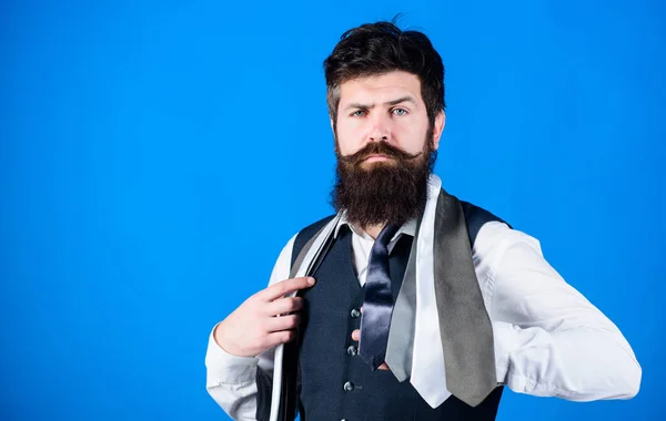 Man bearded hipster hold few neckties on blue background. Guy with beard choosing necktie. Gentlemens guide. How to choose right tie. Classic style. How to match necktie with shirt and suit