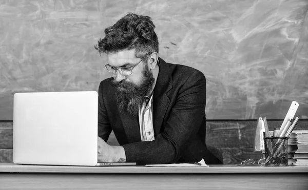 Writing school report. School teacher typing report laptop. Teacher sit at desk with laptop. Back to school concept. Teacher bearded hipster with eyeglasses sit in classroom chalkboard background