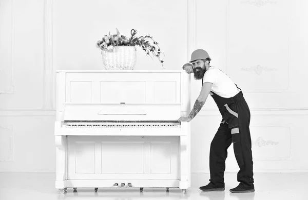Strong worker having a break isolated on white background. Smiling guy with mustache trying to move white piano. Long day at work
