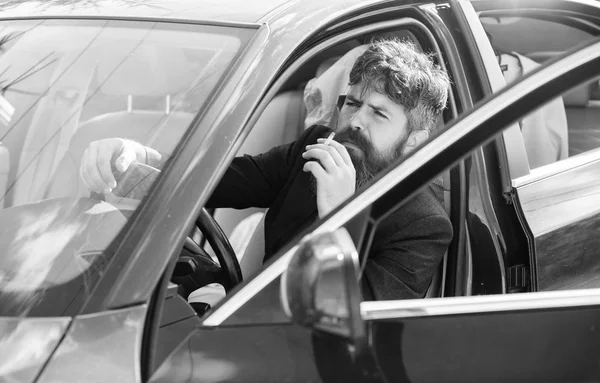 Homem barbudo homem de negócios fumando cigarro enquanto sentado no carro. Condutor a fumar cigarro. Um minuto para relaxar. Empresário cansado após duras negociações de fumar veículo. Proibições de fumar em veículos particulares — Fotografia de Stock