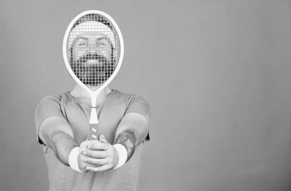 Athlete hipster hold tennis racket in hand red background. Man bearded hipster wear sport outfit. Tennis player beginner retro fashion. Tennis sport and entertainment. Concentrated on tennis court