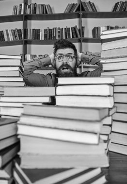 Öğretmen ya da öğrenci sakallı gözlük takmaz, defocused kitaplar ile masada oturur. Adam kazık kitap kütüphane, kitap rafı arka plan üzerinde arasında şok yüzünde. Bilimsel bir keşif kavramı