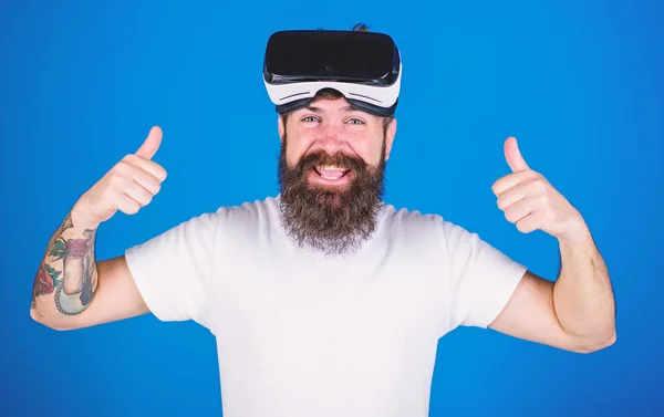 Mann mit Bart und fröhlichem Gesicht genießt Virtual Reality-Erfahrung. Hipster mit stylischem Bart und breitem Lächeln freuen sich über neues VR-Headset. bärtiger Mann zeigt auf blauem Hintergrund vereinzelt die Daumen nach oben — Stockfoto