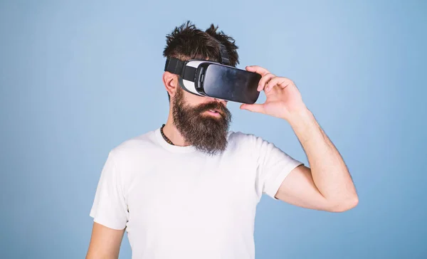 Homem com barba em óculos VR, fundo azul claro. Conceito de dispositivo VR. Cara com cabeça montada exibir interagir em realidade virtual. Hipster em face séria usar gadget moderno para explorar a realidade virtual — Fotografia de Stock